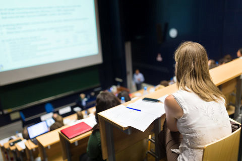 Studierende sitzt in großem Hörsaal und besucht eine Vorlesung